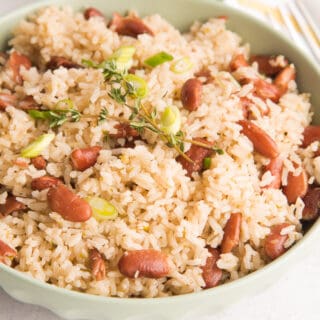 Horizontal image of a light green bowl of Jamaican-Inspired Rice and Peas garnished with fresh thyme.