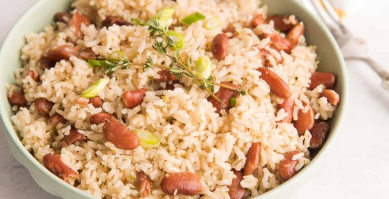 Horizontal image of a light green bowl of Jamaican-Inspired Rice and Peas garnished with fresh thyme.