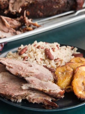Horizontal image of a plate with slices of Jerk Pernil, sweet plantains and rice and peas.