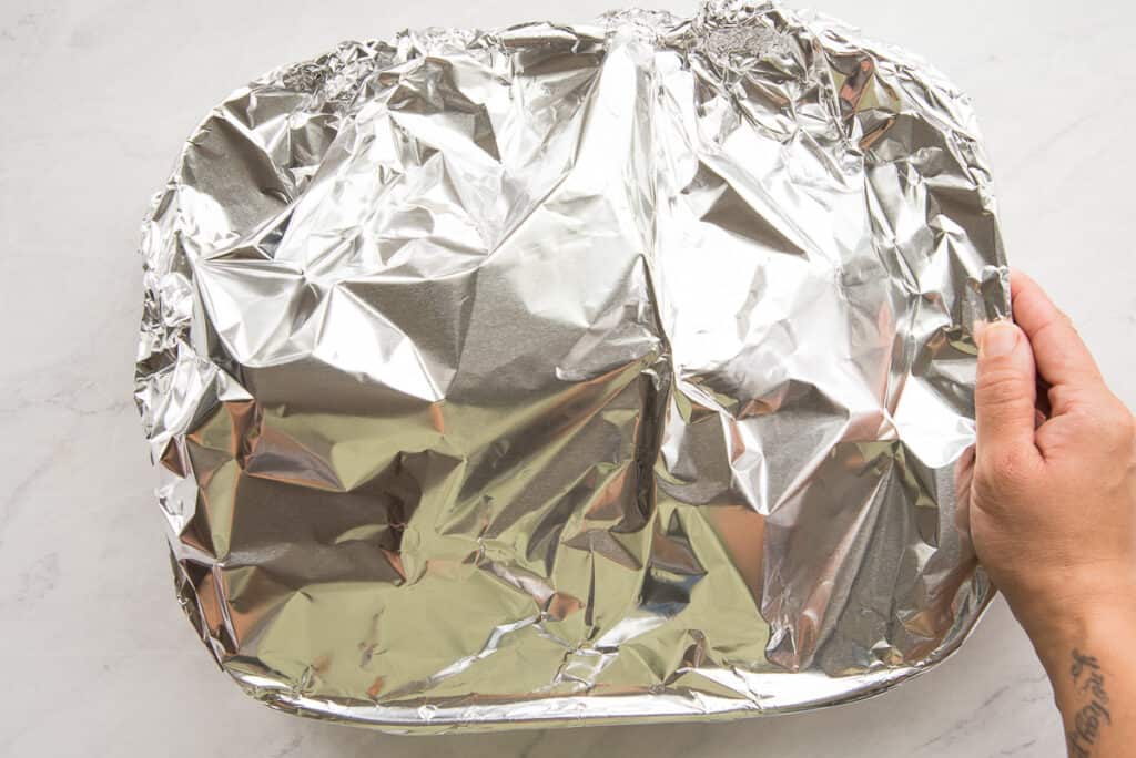 The marinated pork shoulder is loosely covered in foil.