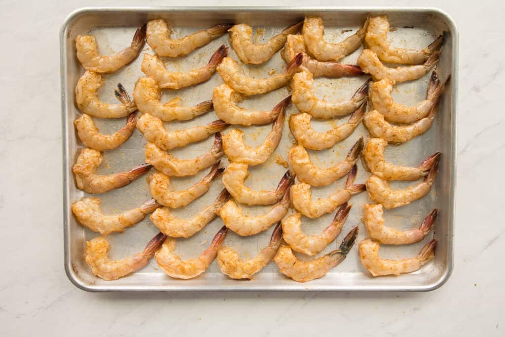 Shrimp arranged on a metal sheet pan before being roasted.