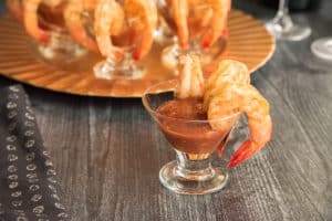 Preview image of a small appetizer glass with cocktail sauce and three roasted shrimp hanging off the right side of the glass rim.