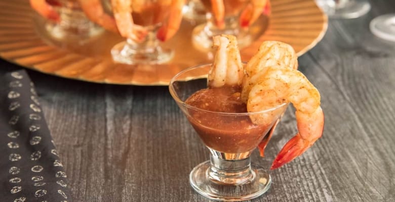 Preview image of a small appetizer glass with cocktail sauce and three roasted shrimp hanging off the right side of the glass rim.