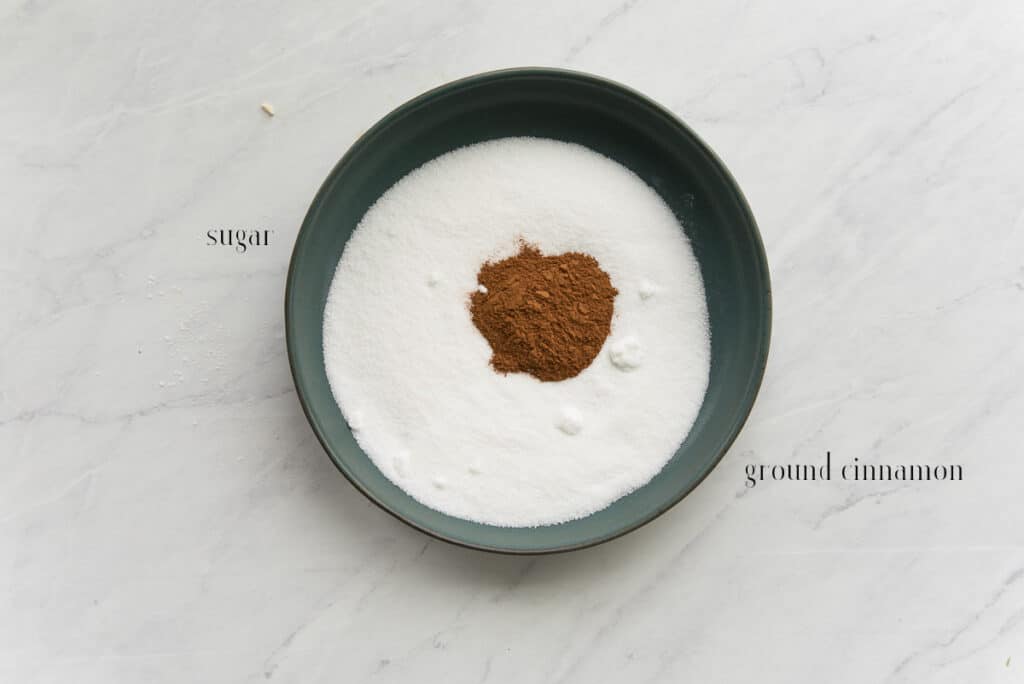 Ingredients needed to make the cinnamon-sugar topping in a green ceramic bowl: cinnamon and sugar.