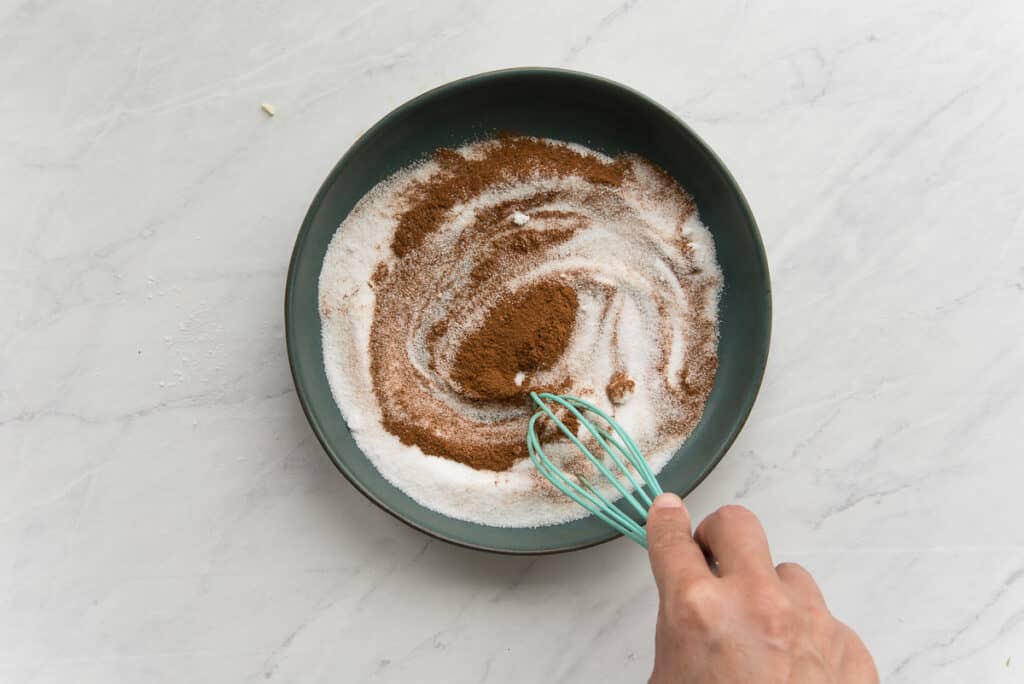 The cinnamon and sugar are whisked together in a wide shallow green ceramic bowl.