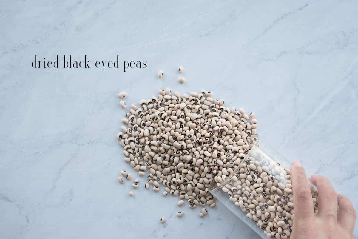 Black eyed peas are poured from a container onto a white counter to be sorted.