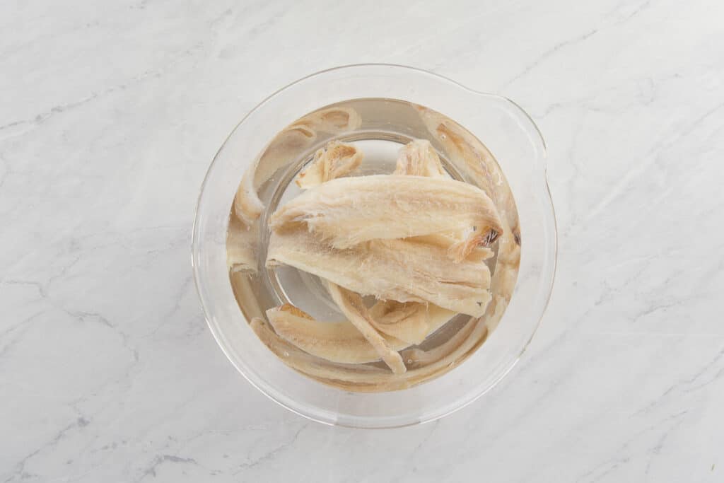 The codfish is desalinated in cold water in a clear glass bowl.