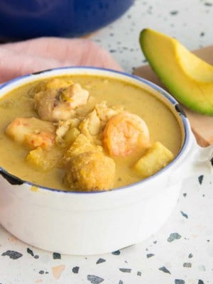 FB social media image of Caldo Santo in a white bowl next to a wooden cutting board with a slice of avocado on it.