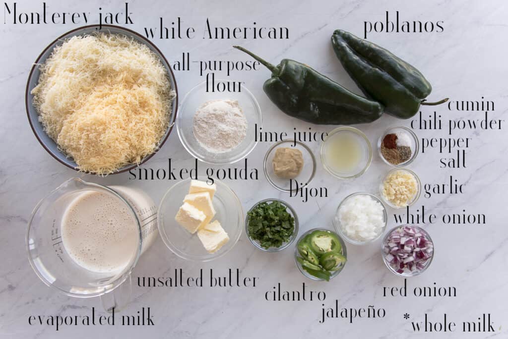 Ingredients to make the Roasted Poblano White Queso Dip monterey jack cheese, white american cheese, smoked gouda, all-purpose flour, poblano peppers, spices, lime juice, dijon mustard, onions, cilantro, jalapeño, butter, and evaporated milk.