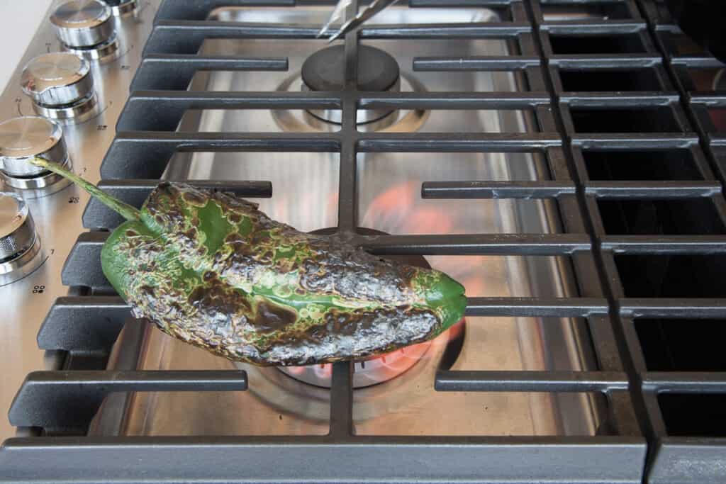 A pepper is charred over the open flame of a gas stove.