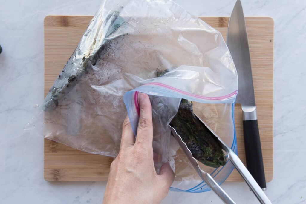 Tongs are used to put the charred pepper into a plastic food storage bag before they are steamed.
