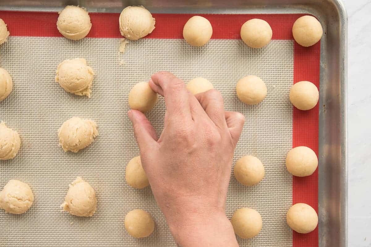 The scoops of cookie dough are rolled into balls and arranged on a red and white silicone baking mat.