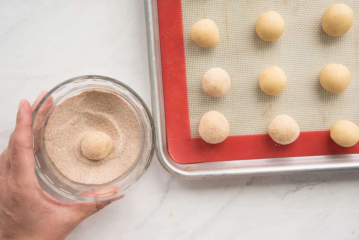 The cookie dough is rolled in cinnamon sugar and put onto a silicone baking mat.
