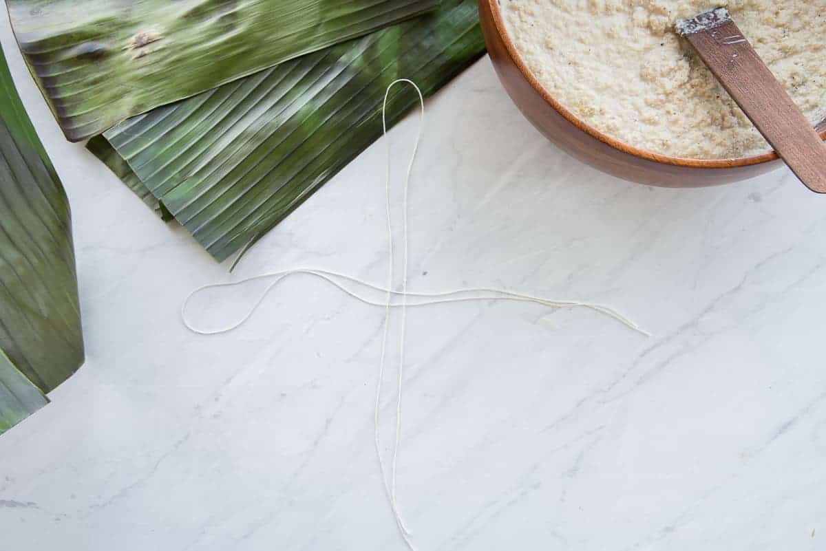 Two pieces of twine are crossed over each other to wrap banana leaf bundles.