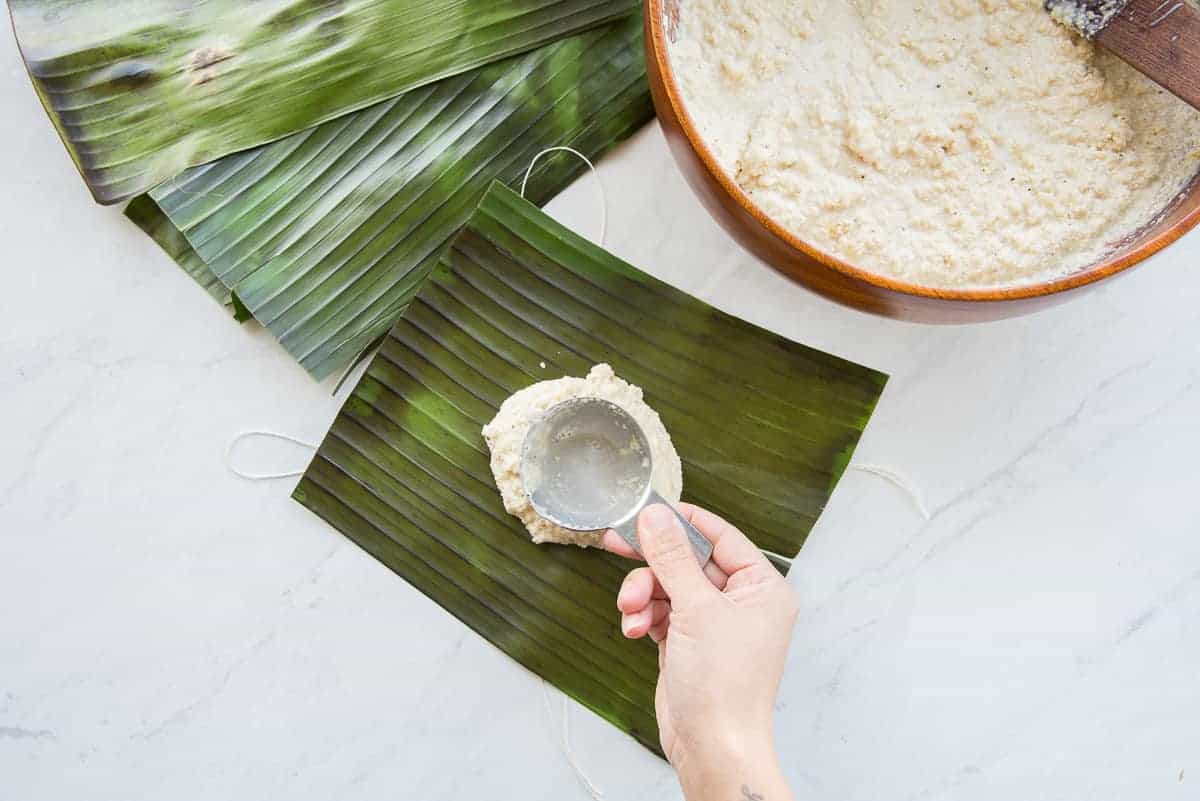 The coconut grits mixture is spooned into the center of a banana leaf square.