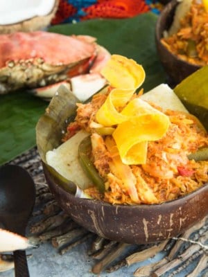 Social media image of a coconut bowl filled with Salmorejo de Jueyes with Coconut Grits Cakes topped with a fried plantain.
