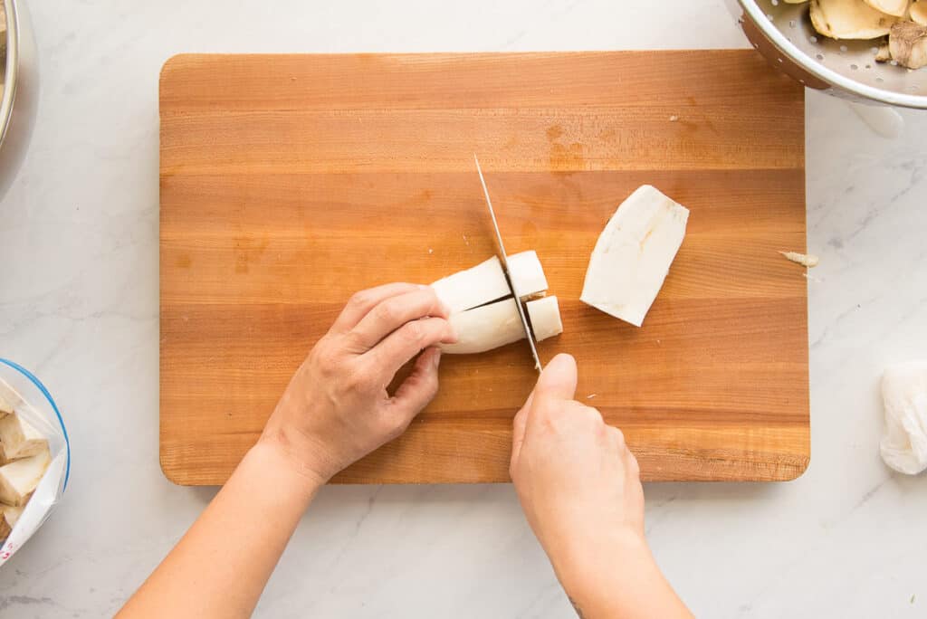 The yuca is cut into 1-inch cubes on a wooden cutting board.