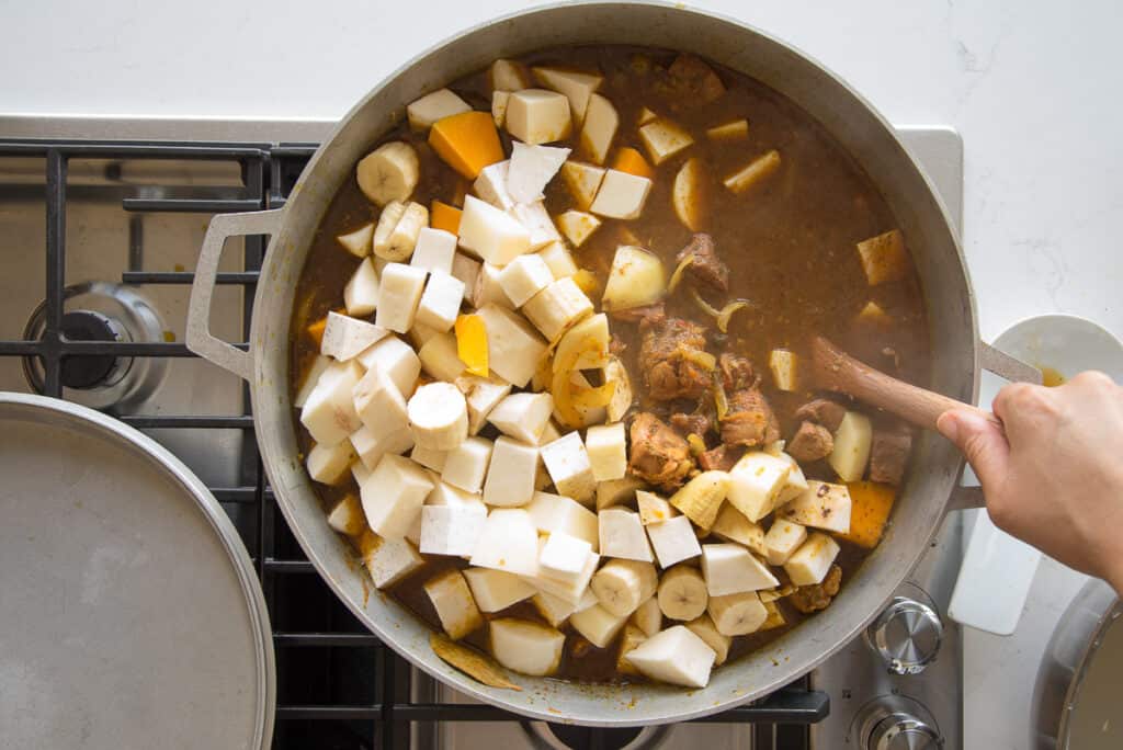 The root vegetables are stirred into the ingredients in the caldero with a wooden spoon.