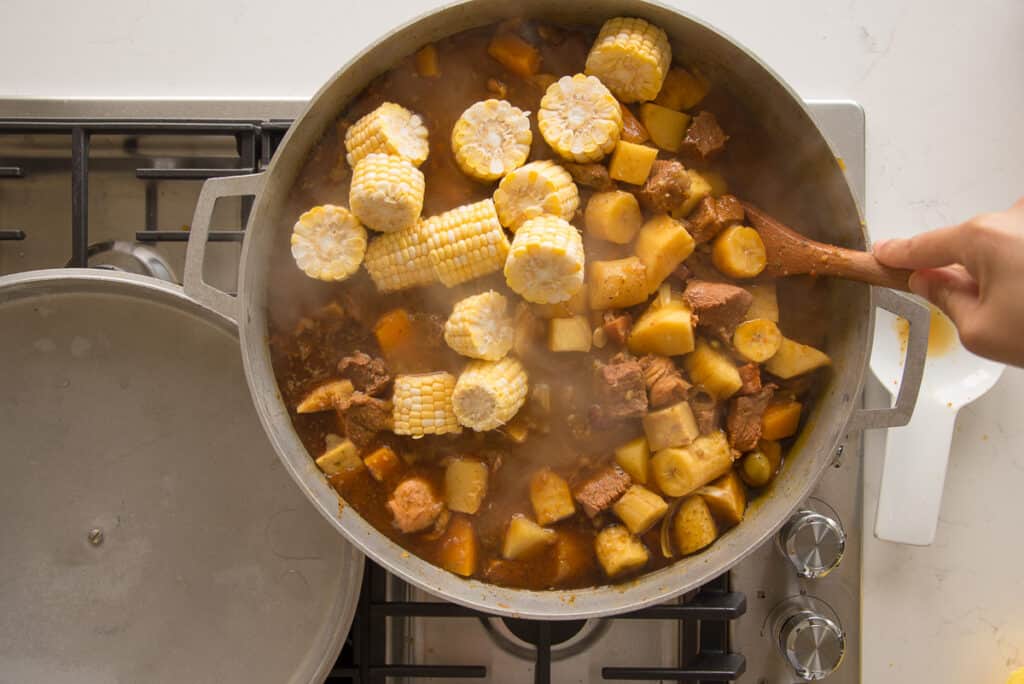 The sweet corn slices are stirred into the stew with a wooden spoon.