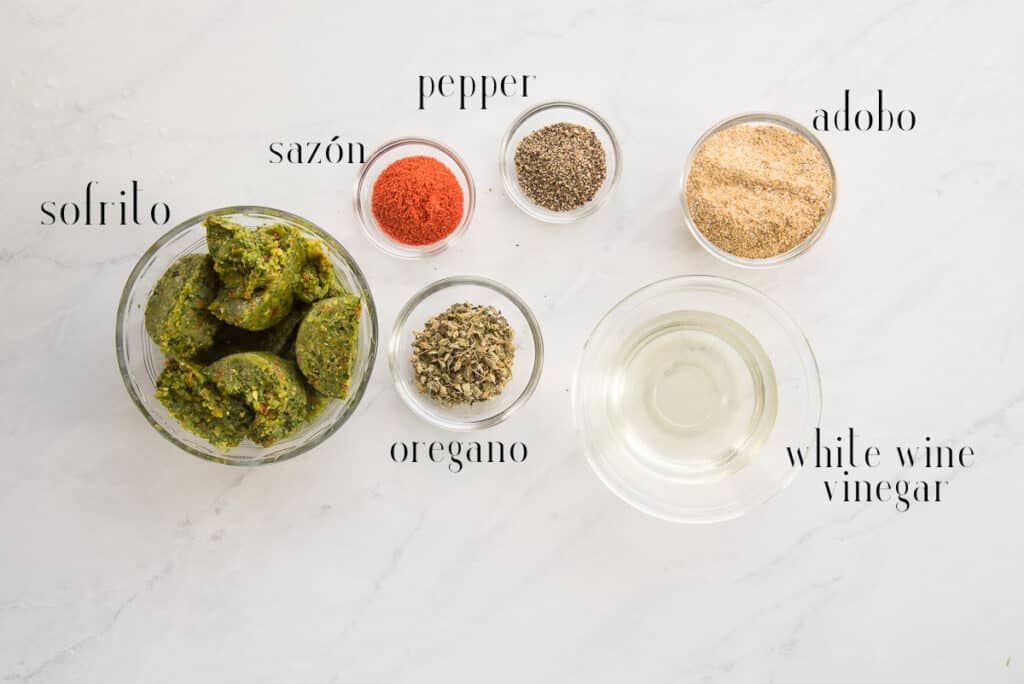 Ingredients for the meat marinade are pictured sofrito, sazón, peppe, oregano, adobo, and white wine vinegar