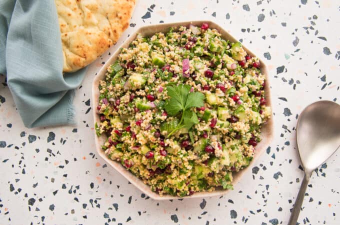 Preview image of a pink bowl of bulgur garnished with parsley next to a pile of naan wrapped in blue fabric.