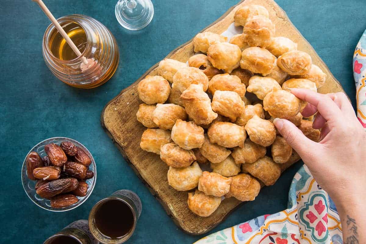 A hand places a date bite onto a pile of Goat Cheese Stuffed Dates in Puff Pastry