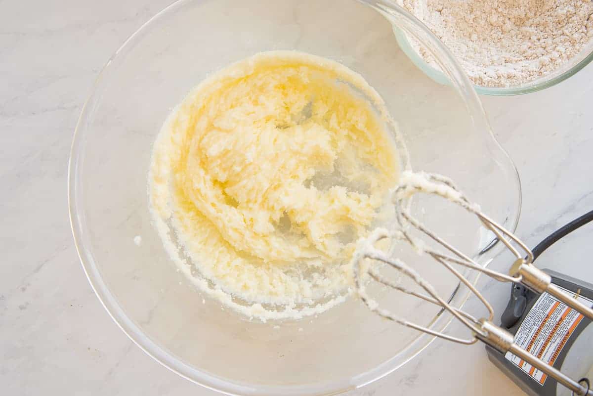 The butter and sugar are beaten together in a glass mixing bowl.