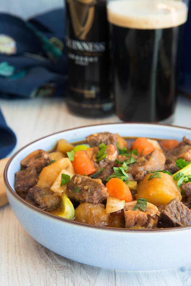 Close up of a blue bowl of Guinness Beef Stew in front of a glass of Guinness.