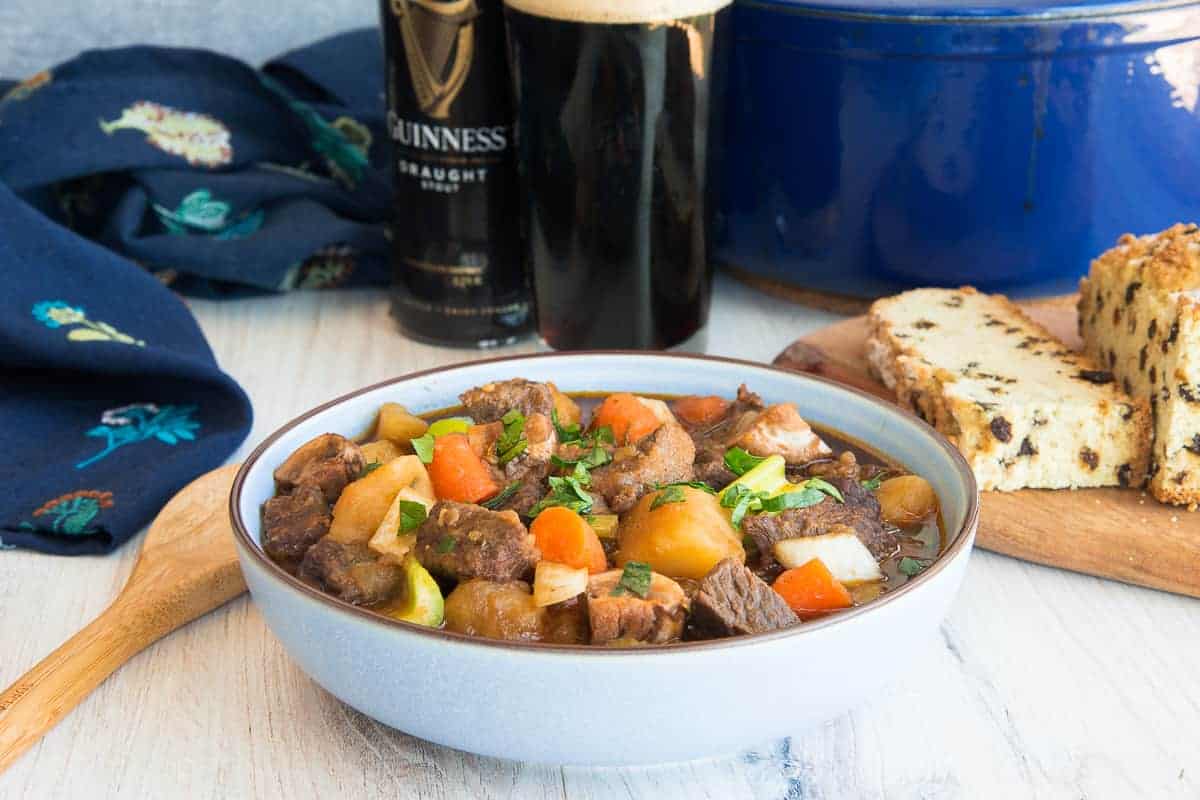 Guinness Beef Stew in a blue bowl next to a slice of bread on a cutting board.
