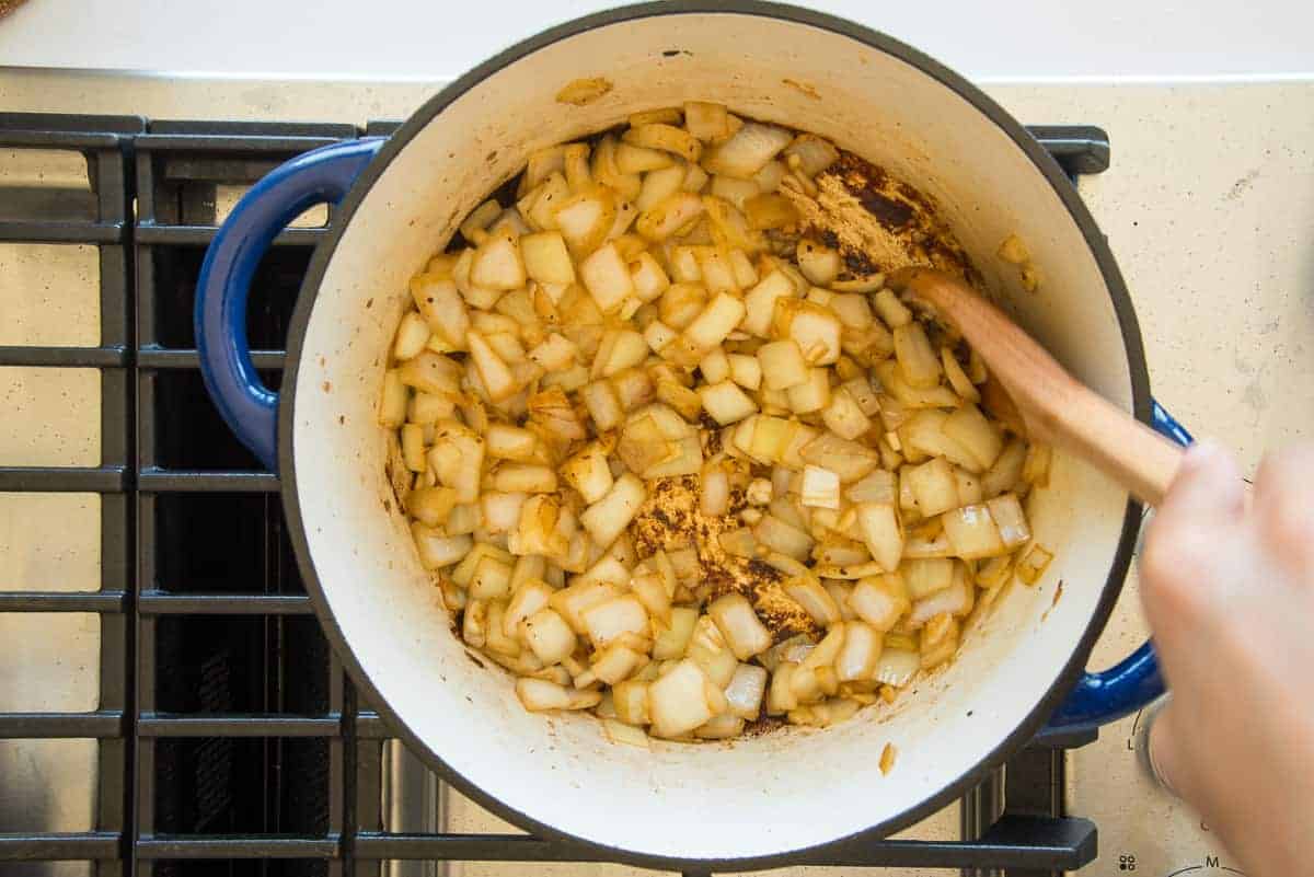 Onions and garlic are sauteed until golden in a blue pot on a stove.