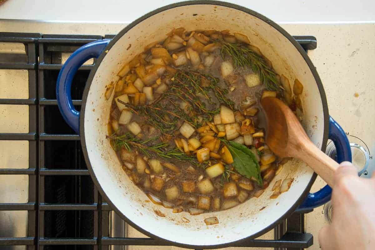 A spoon stirs the herbs into liquid in the pot on a stove.