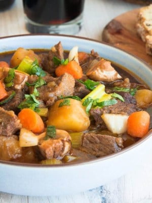 Side view of a blue bowl of Guinness Beef Stew next to a slice of bread.