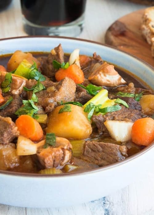 Side view of a blue bowl of Guinness Beef Stew next to a slice of bread.