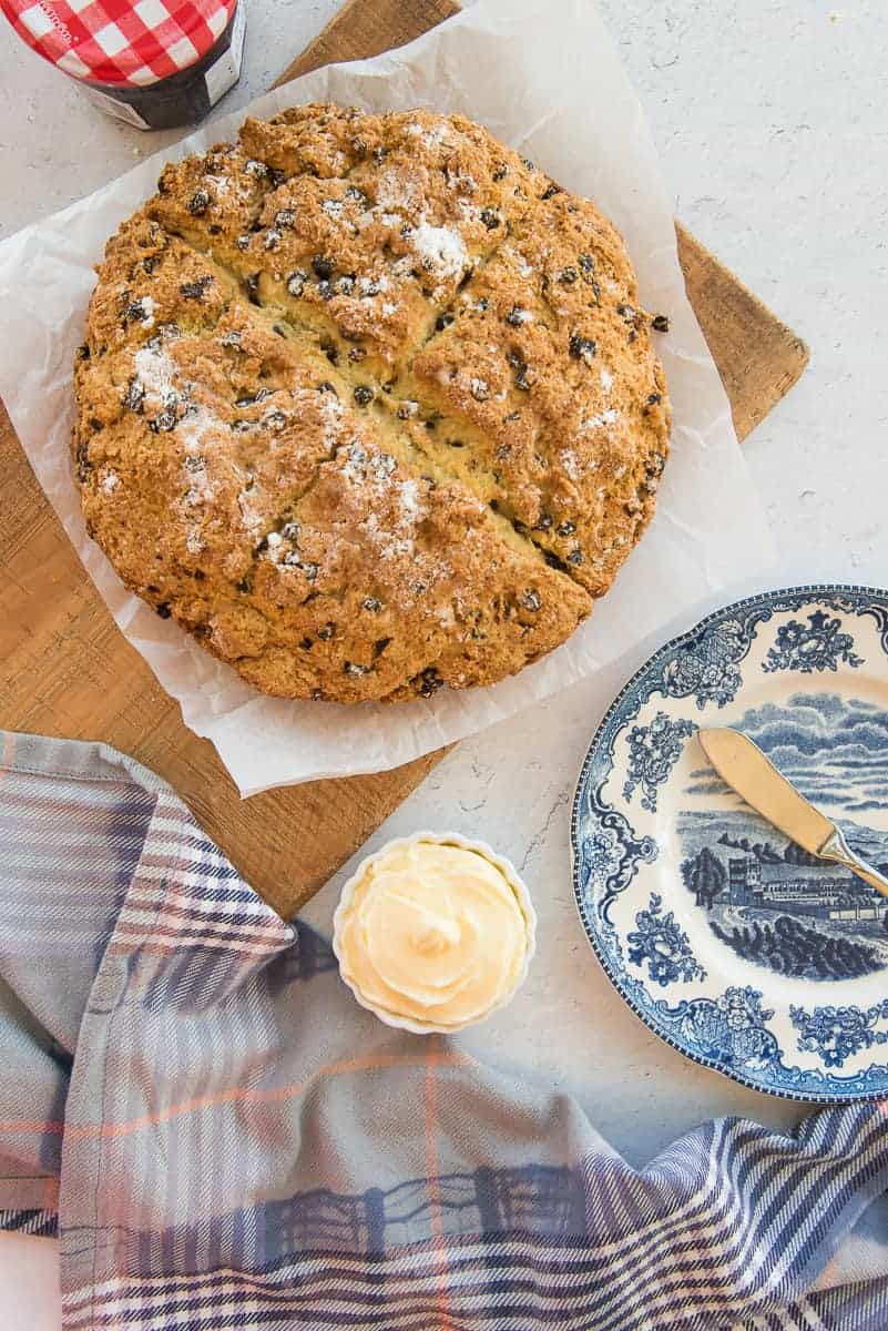 The baked loaf of Irish Soda Bread is on a wooden board next to a small bowl of butter.