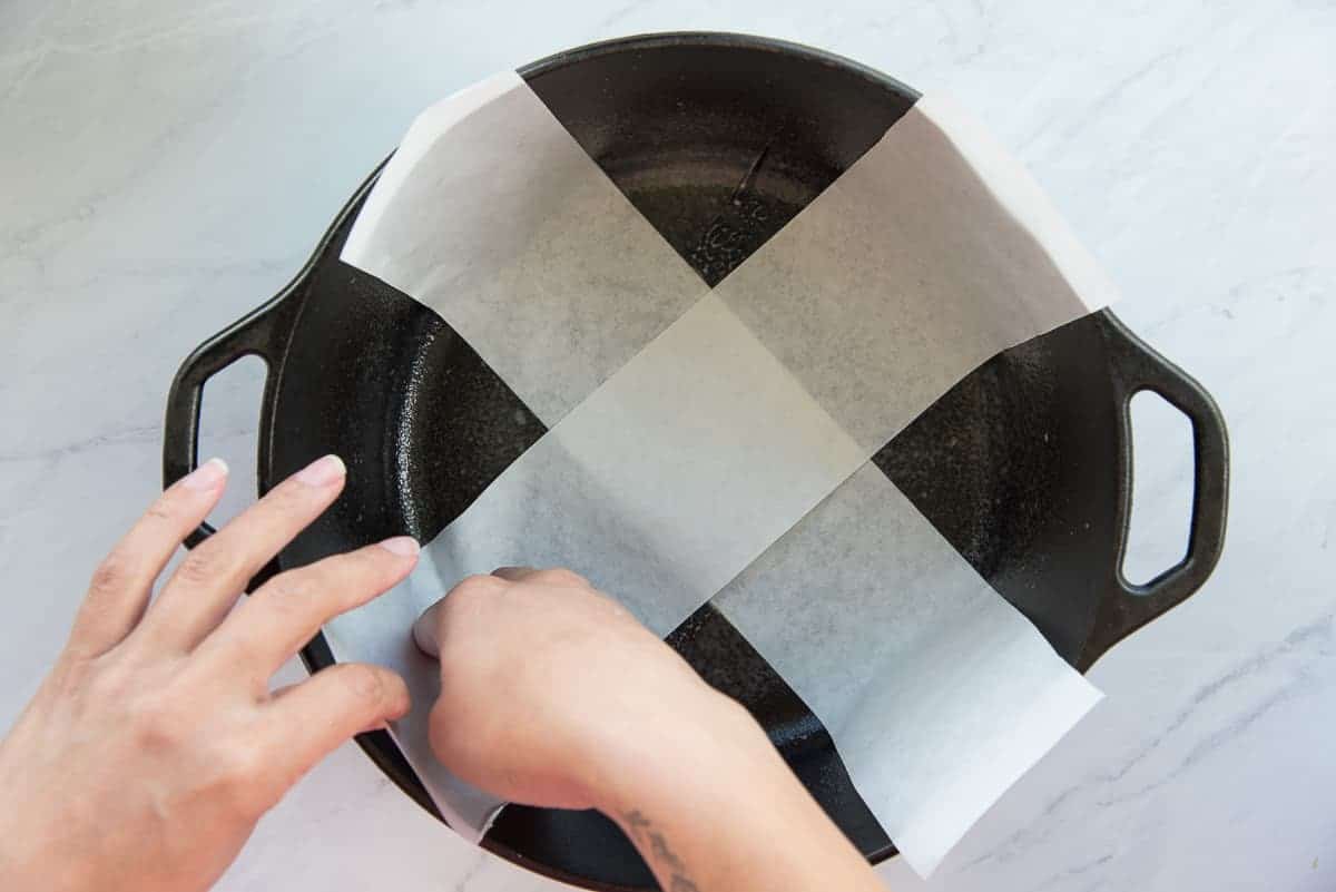 Hands criss cross strips of parchment in a cast iron dutch oven.