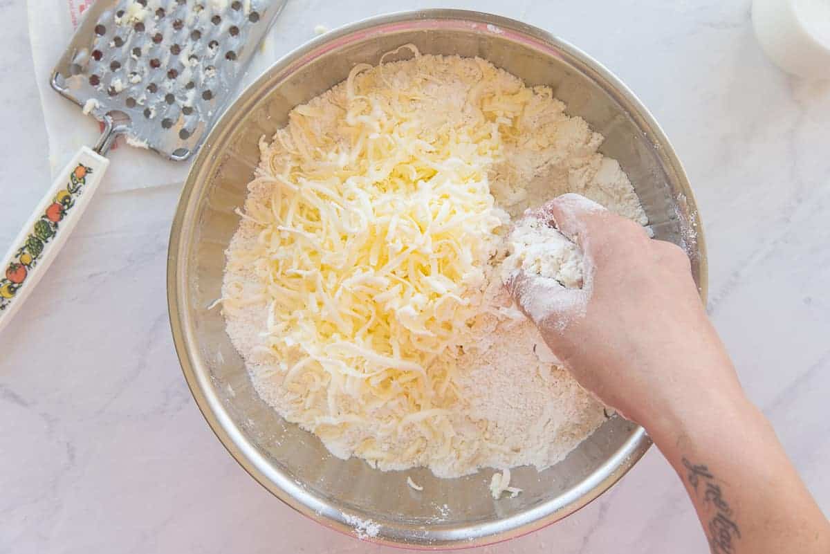 A hand cuts the shredded butter into the dry ingredients in a mixing bowl.