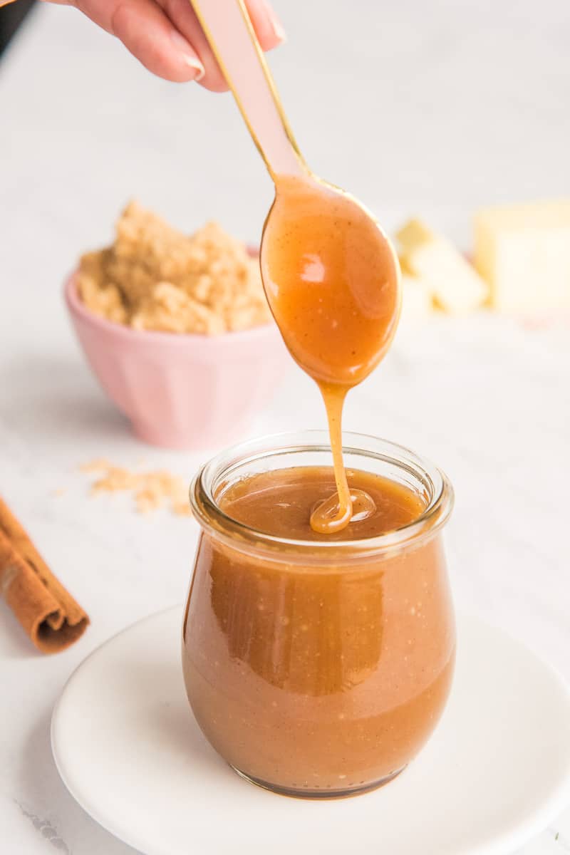 Pink spoon drips Spiced Toffee Sauce back into its glass jar container.