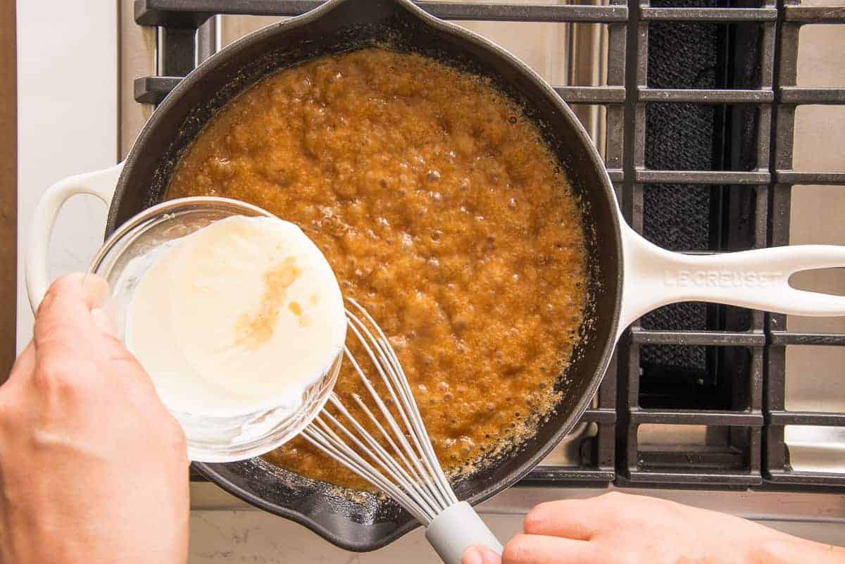 Warm cream is added to the sugar mixture in a white sauté pan.