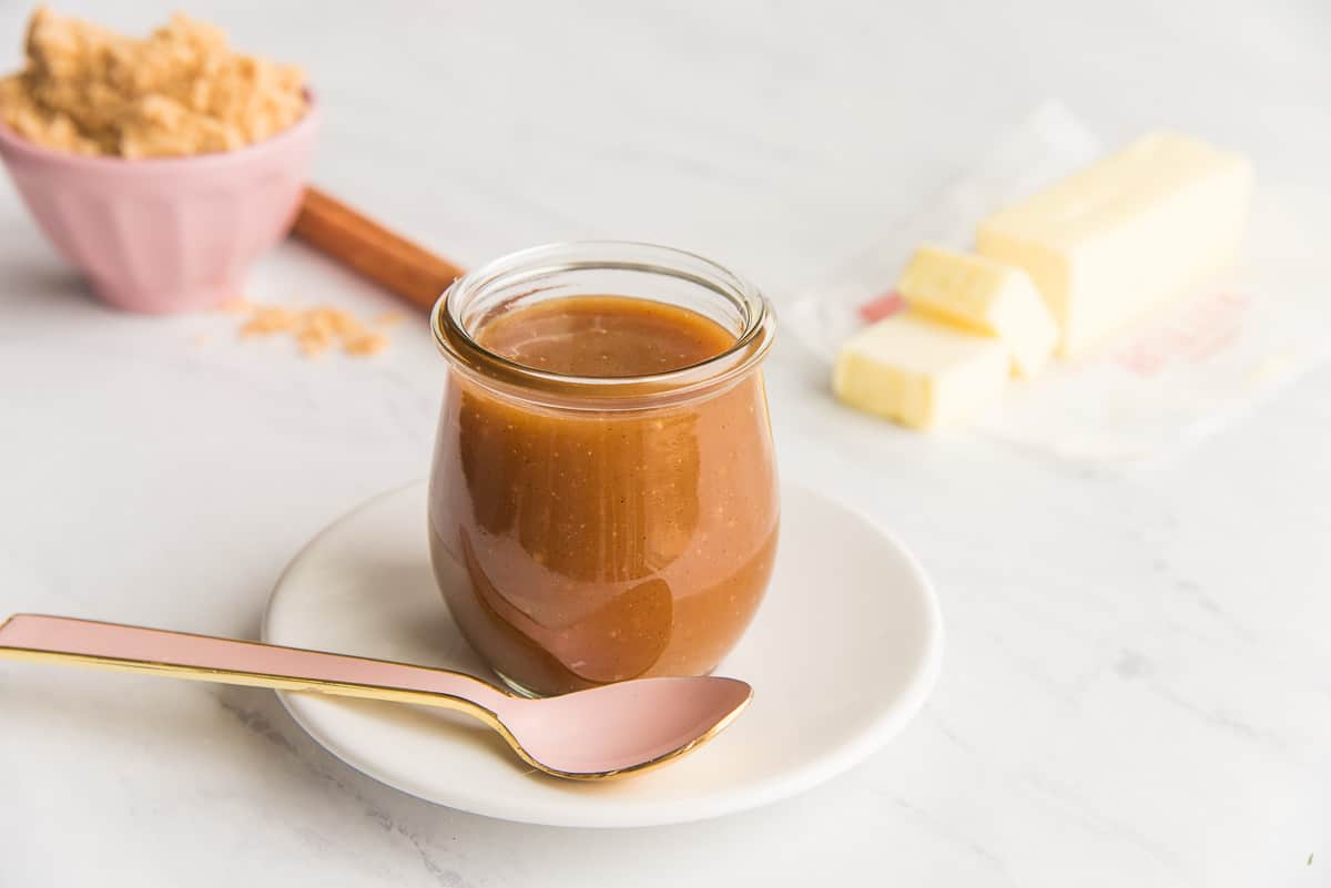 A glass jar of Spiced Toffee Sauce on a white plate.
