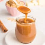 A pink spoon lifts Spiced Toffee Sauce from a small glass jar