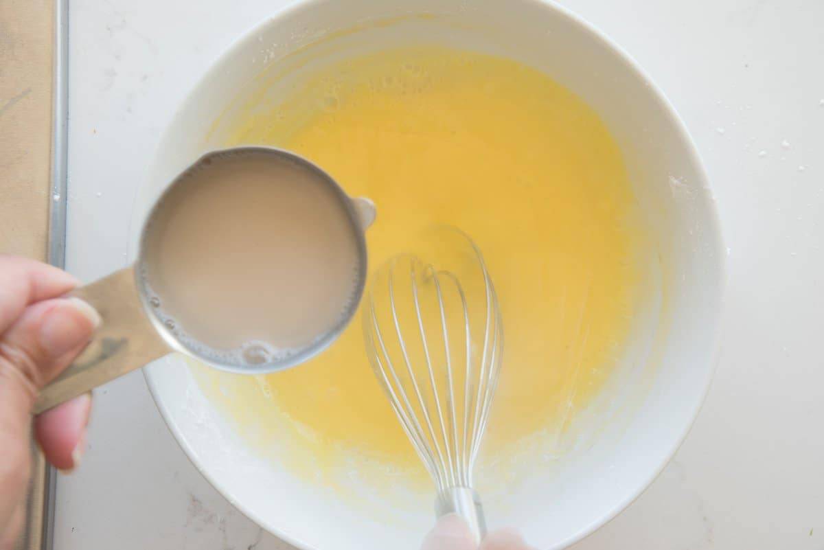 The hot milk mixture is whisked into the eggs to temper them.