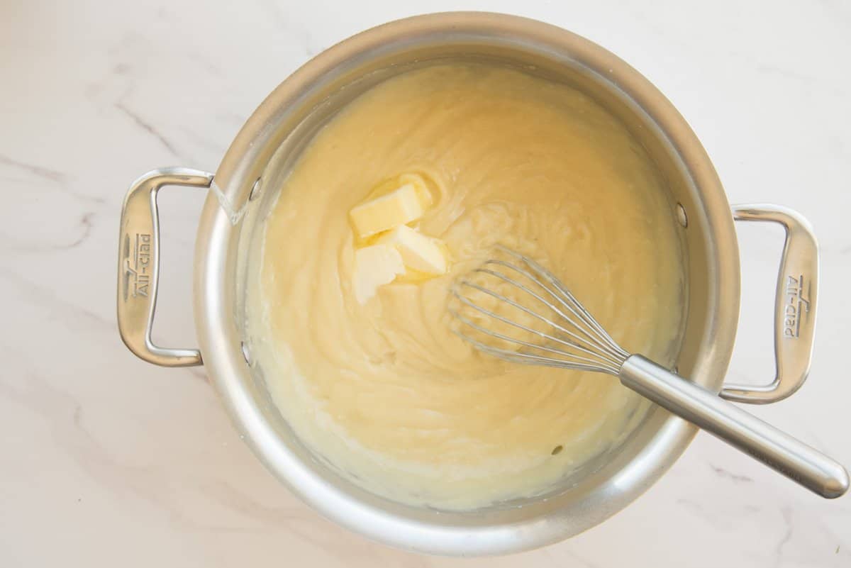 Butter is whisked into the custard in a silver pot.
