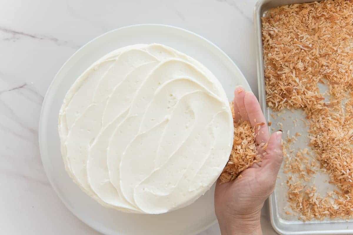 A hand pressed the toasted coconut flakes onto the side of the cake.