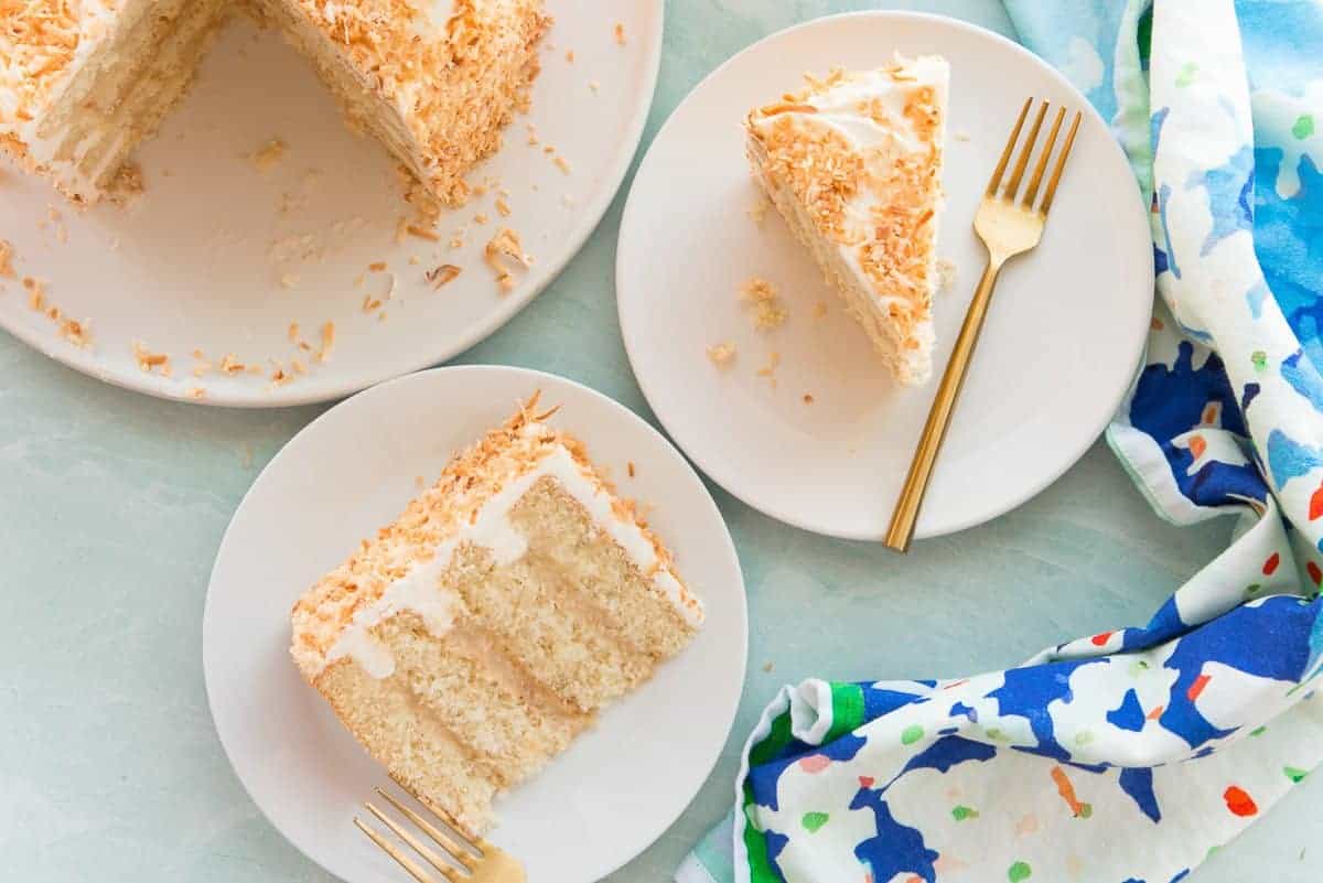 Two slices of Toasted Coconut Cake on white plates on a green surface.