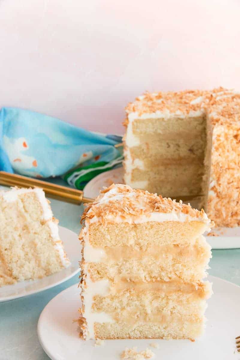 A slice of Toasted Coconut Cake on a white plate that reveals the layers.