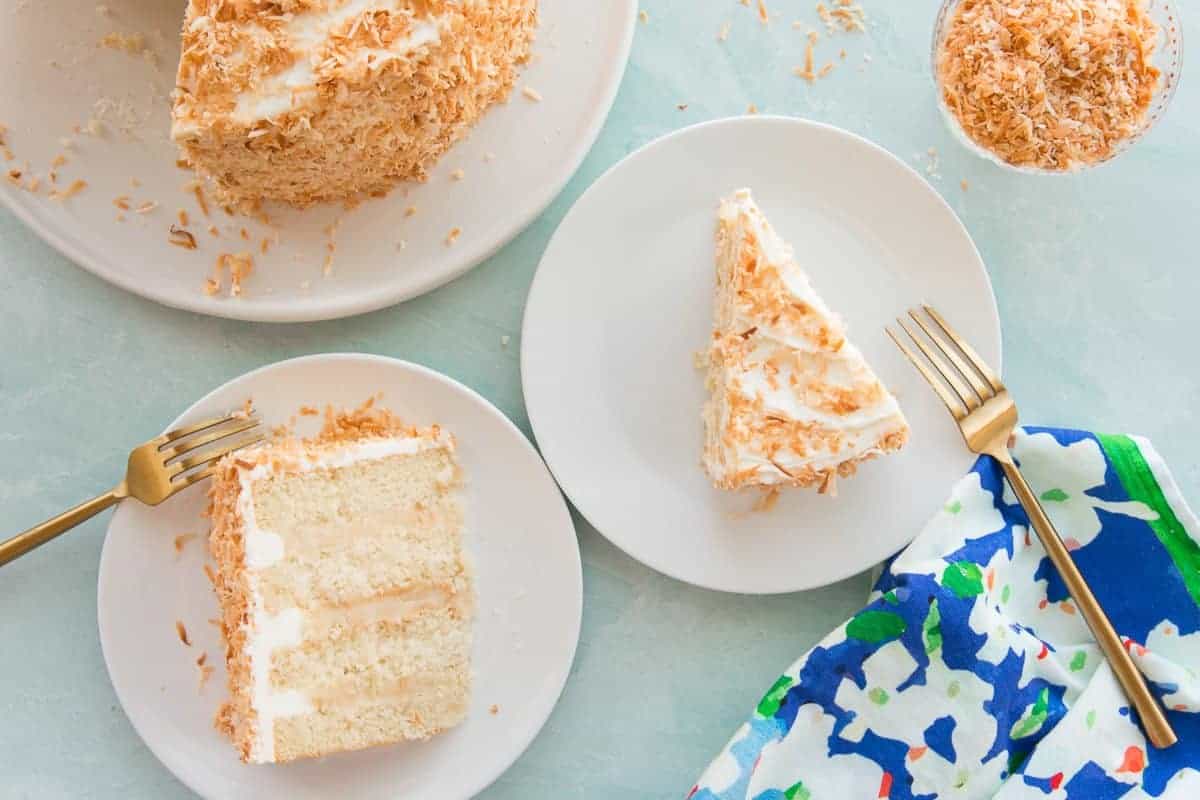 One slice of Toasted Coconut Cake laying down on a white plate next to a slice standing up.