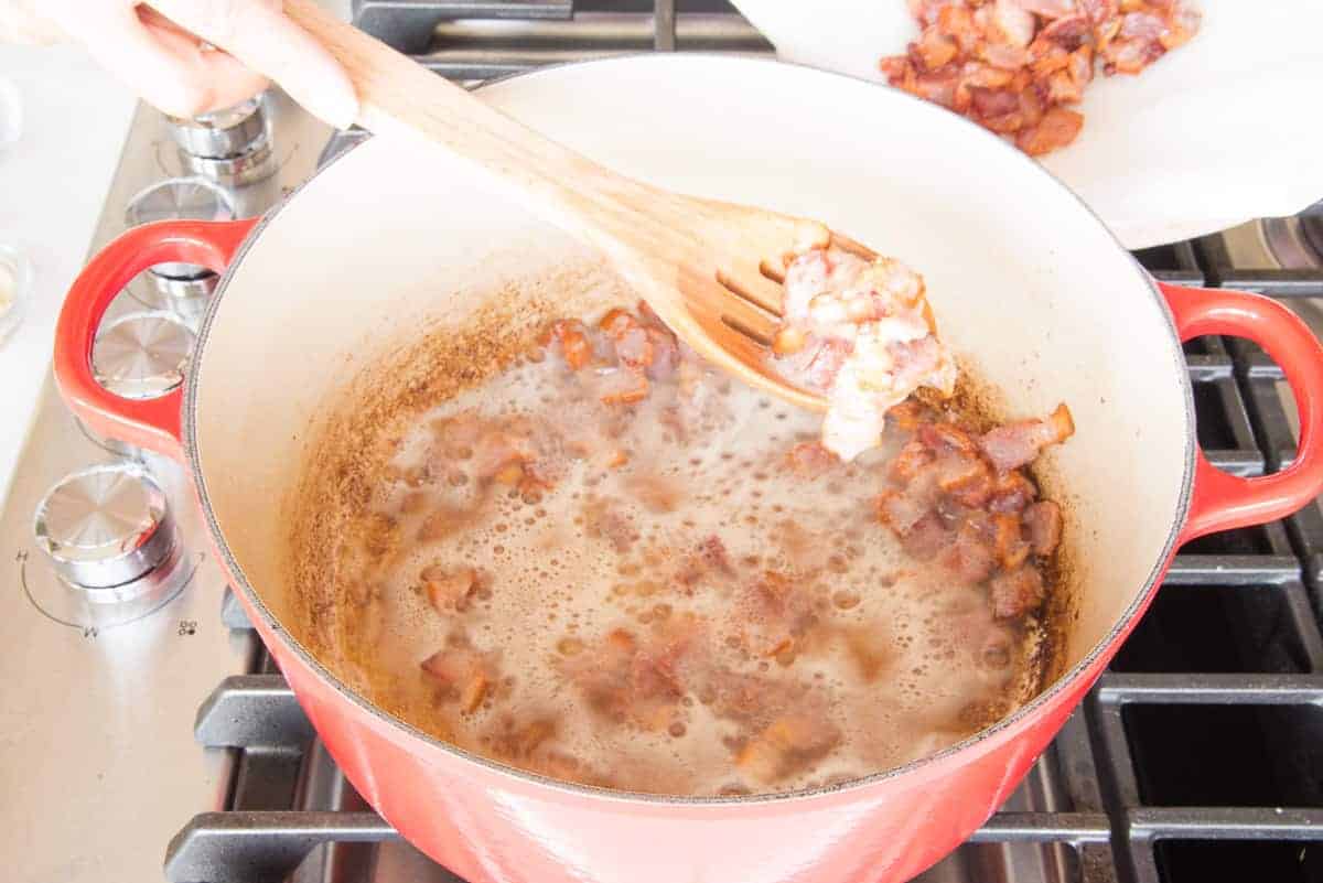 Bacon is removed from the pot with a slotted wooden spoon.