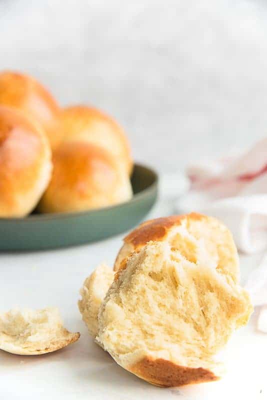 A bowl of Brioche Rolls with one in front torn in half to reveal fluffy interior.