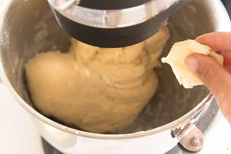 Butter is pinched before being added to the dough being kneaded in the mixing bowl.