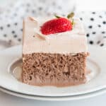 A piece of Chocolate Tres Leches Cake with chocolate whipped cream garnished with a fanned strawberry.